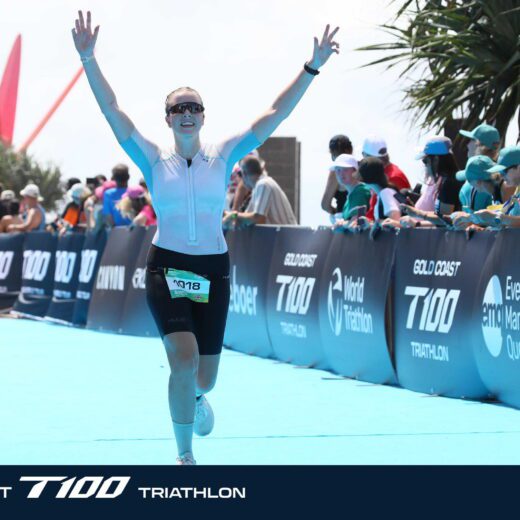 Sophie Dyer crossing the finish line at T100 triathlon with arms raised in celebration