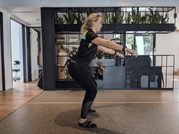 Squatting with stiff ankles showing altered movement mechanics and reduced ankle mobility